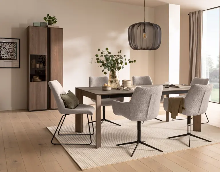 Modernes Esszimmer mit dunklem Holztisch, sechs grauen Polsterstühlen auf Metallgestellen, großer schwarzer Stoffpendelleuchte und Schrank in Nussbaumoptik